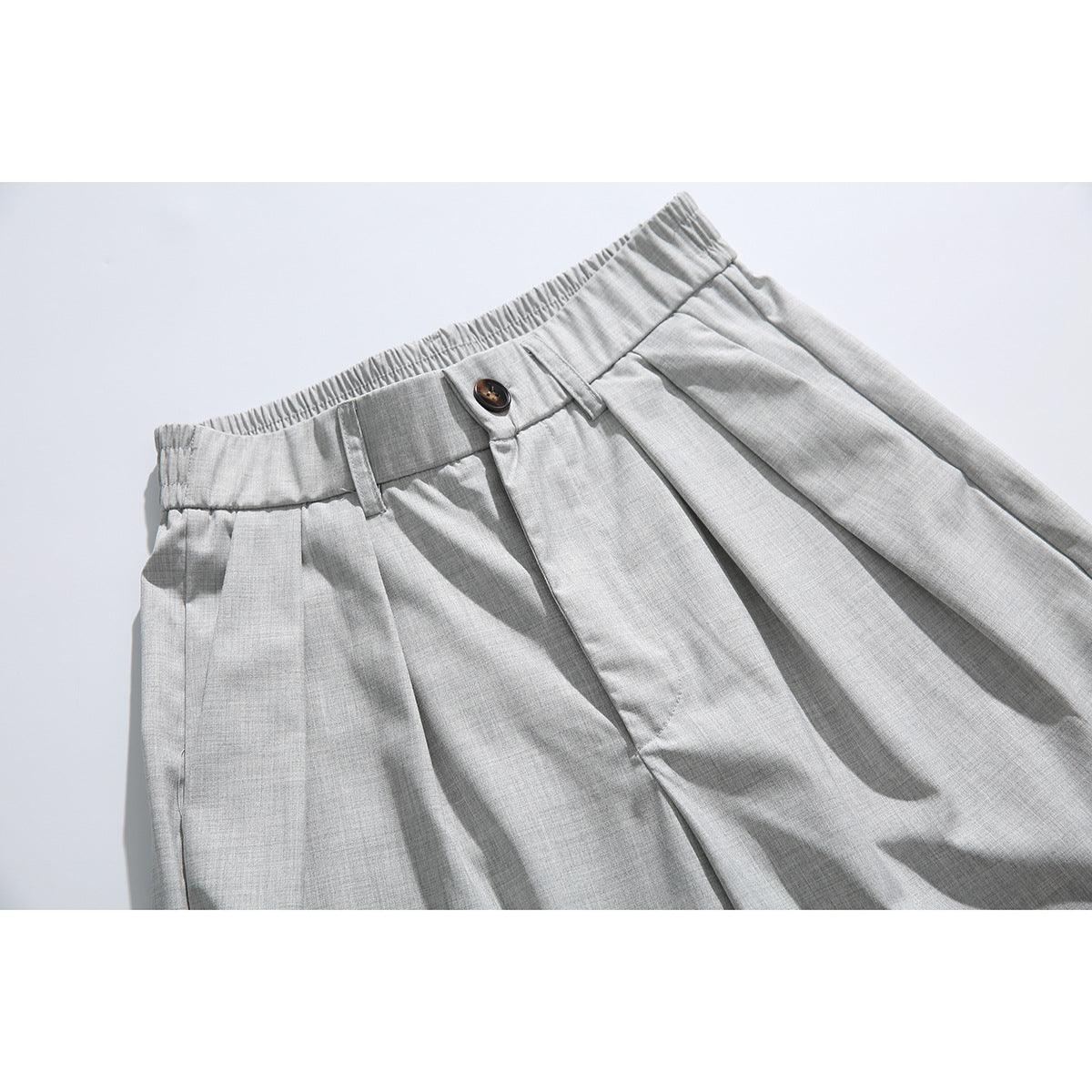 Close-up of light gray tailored shorts showing the elasticized waistband, button, belt loops, and front pleats.