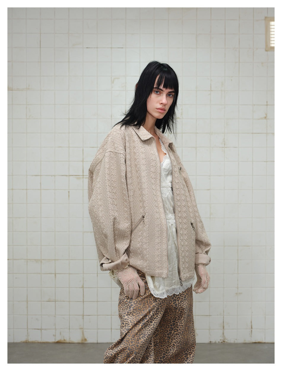 Angled close view of a model wearing a light beige textured zip jacket over a white lace top and leopard-print pants.