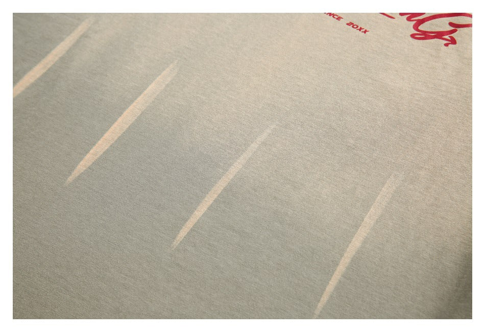 Close-up of muted khaki fabric with pale diagonal marks and a cropped red chest print.