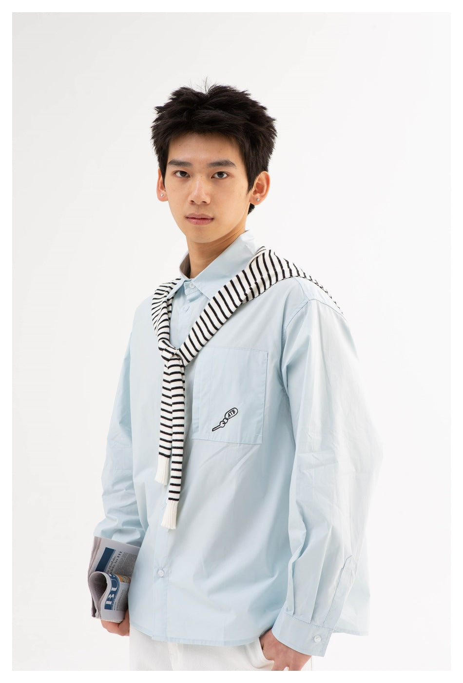 Model wearing a pale blue button-up shirt with a chest pocket and a black-and-white striped sweater draped over the