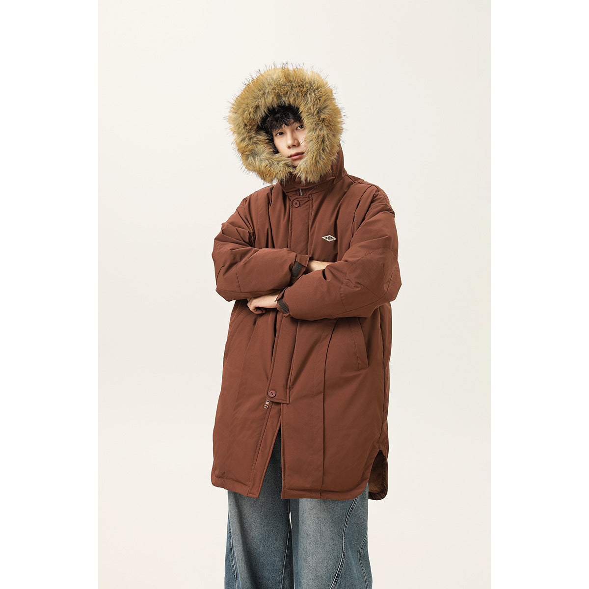 Model wearing a long rust-brown parka with a large tan fur-trimmed hood, shown from the front.