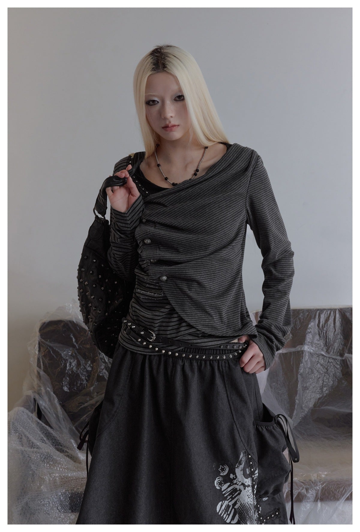 Model wearing a charcoal striped asymmetrical top with draped front, decorative buttons, and long sleeves.