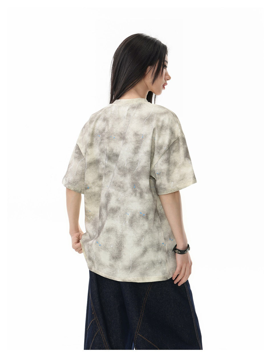 Side and back view of a model wearing a beige-gray mottled oversized T-shirt with scattered flecks.
