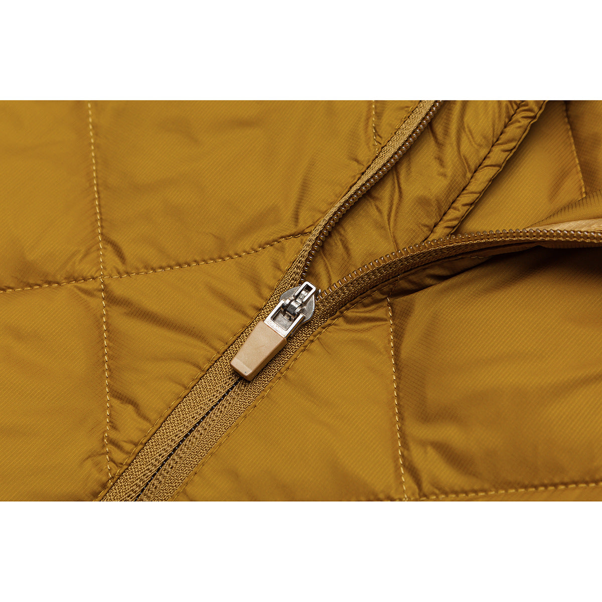 Close-up of a mustard quilted jacket zipper with a light-colored pull tab.