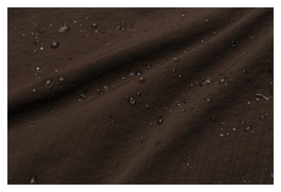 Water droplets bead on dark brown fabric arranged in soft folds.