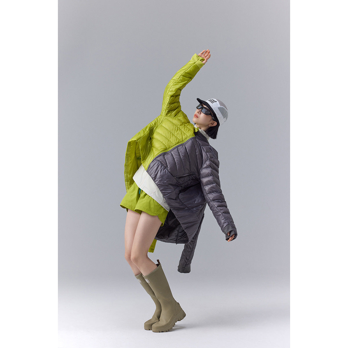 Model in a lime green and charcoal color-block quilted jacket, posing against a plain gray studio background.
