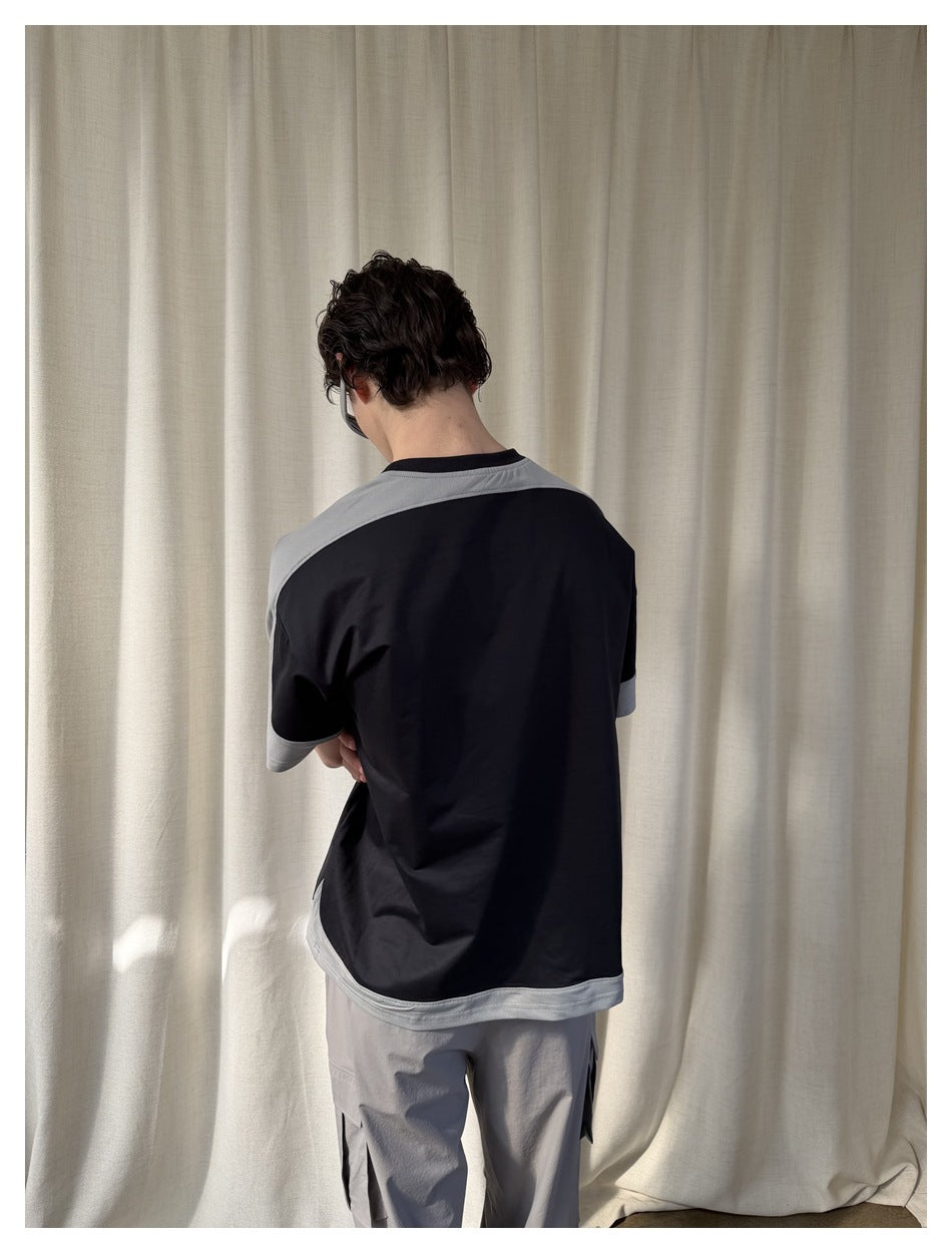 Back view of a model wearing a black T-shirt with light gray shoulder panels, sleeve cuffs, and hem.