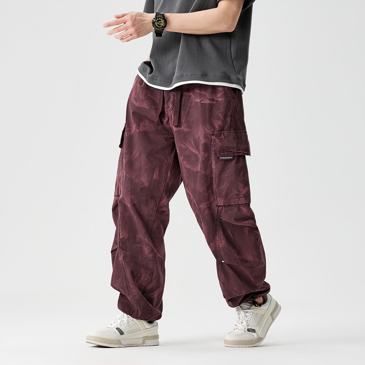 Cropped model wearing loose burgundy cargo pants with multiple flap pockets and gathered ankles, shown from the front.