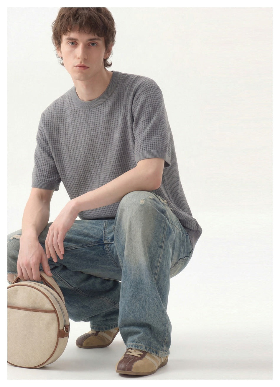 Seated model wearing a gray textured short-sleeve crewneck top and loose blue jeans.