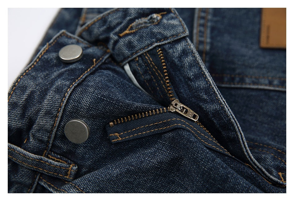 Close-up of dark blue jeans with the metal fly zipper and waistband button visible.
