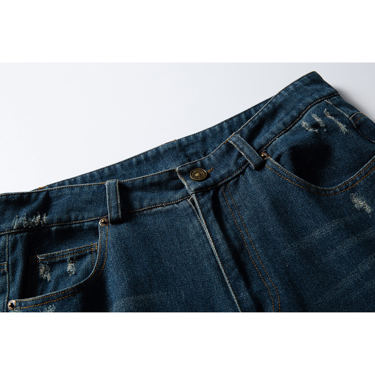 Close-up of the front waist and pockets of dark blue distressed jeans with a metal button and orange stitching.