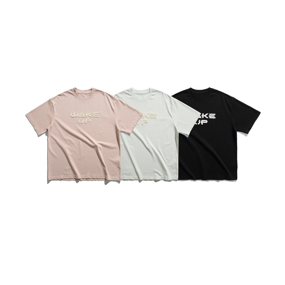 Three short-sleeve crew-neck T-shirts displayed together in blush pink, pale mint, and black, each with front lettering.
