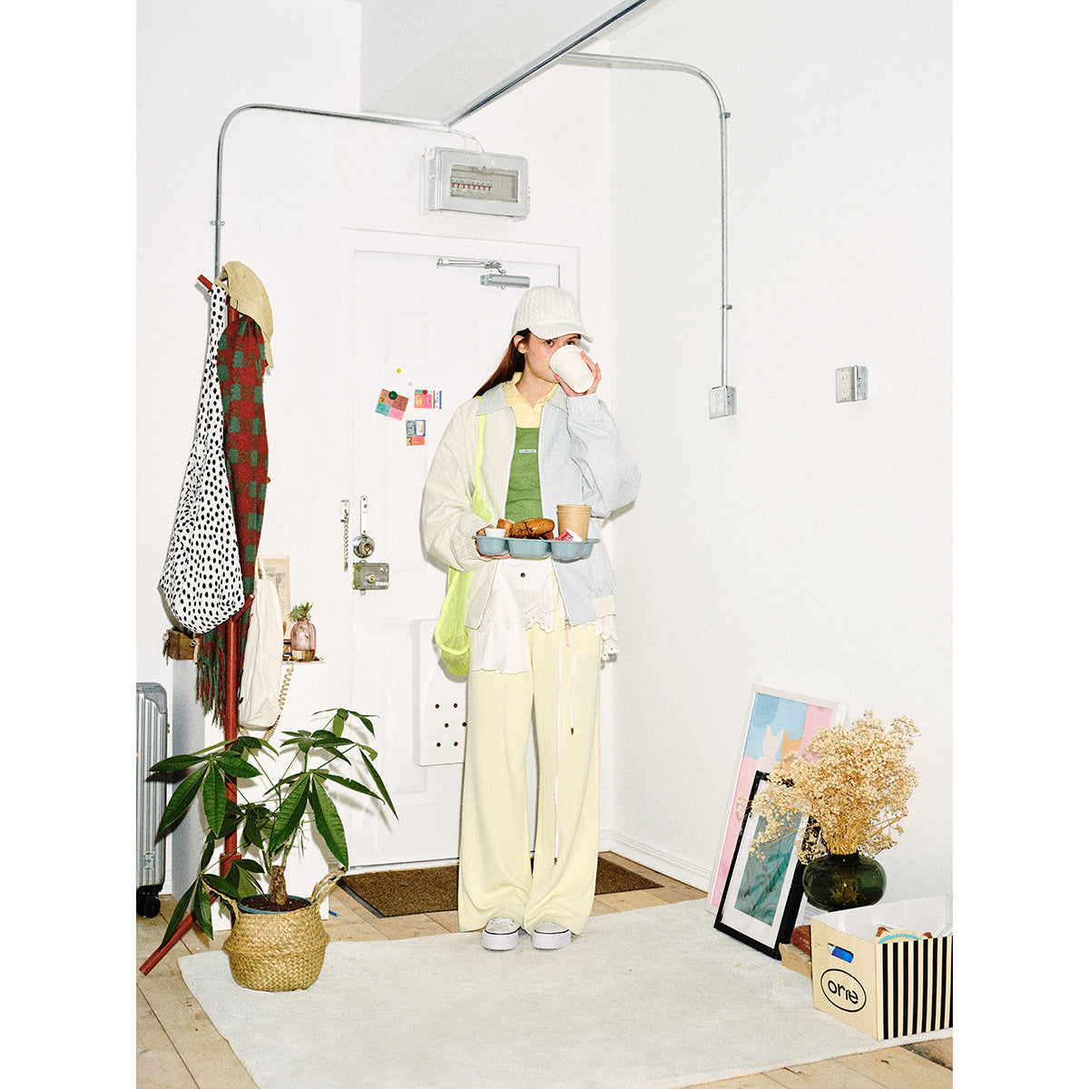 Full-length model wearing a two-tone pinstriped jacket and cream trousers while drinking from a cup.