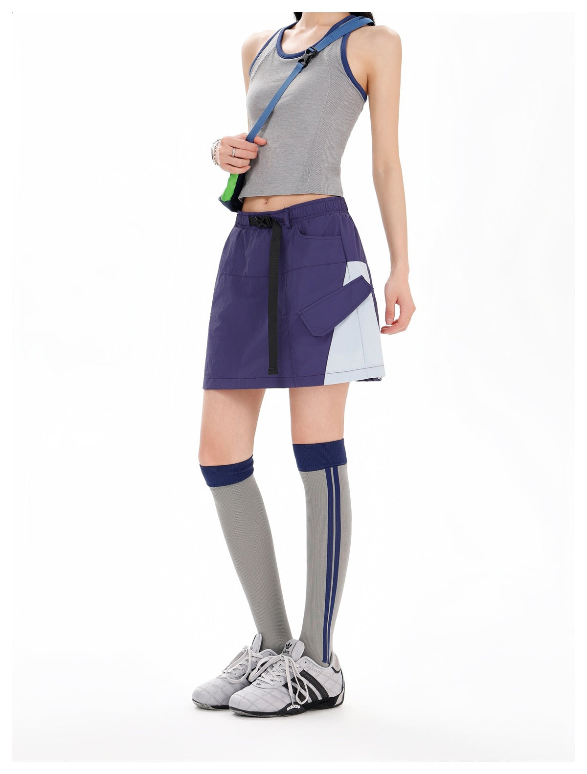 Model wearing a purple utility mini skirt with a pale gray side panel, flap pockets, and a black belt.