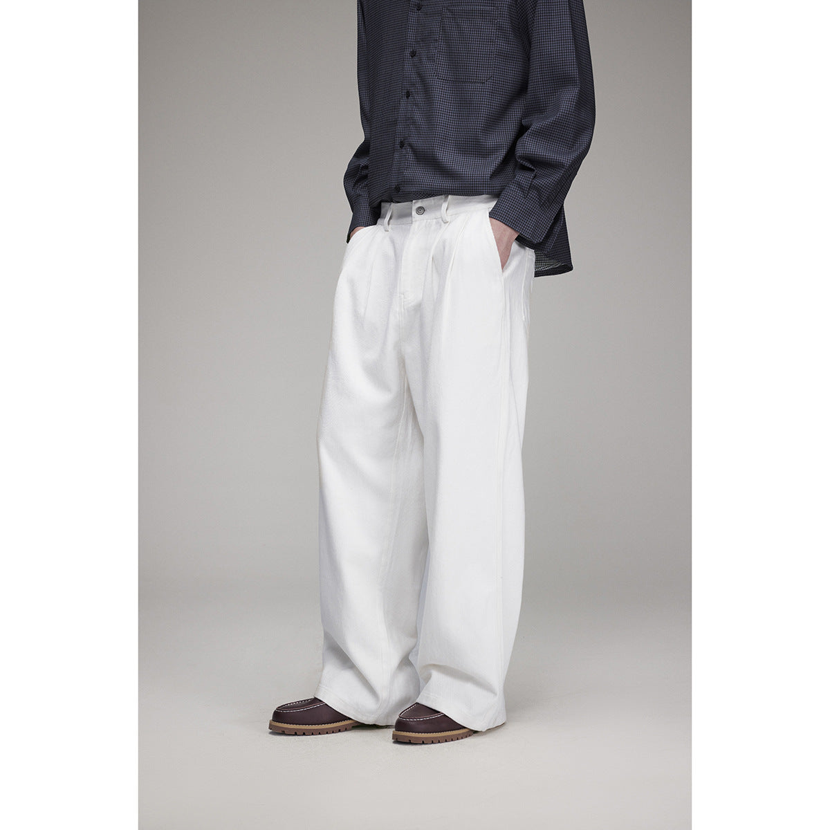 Model wearing white wide-leg pleated trousers with a dark checked shirt, shown from the front at an angle.