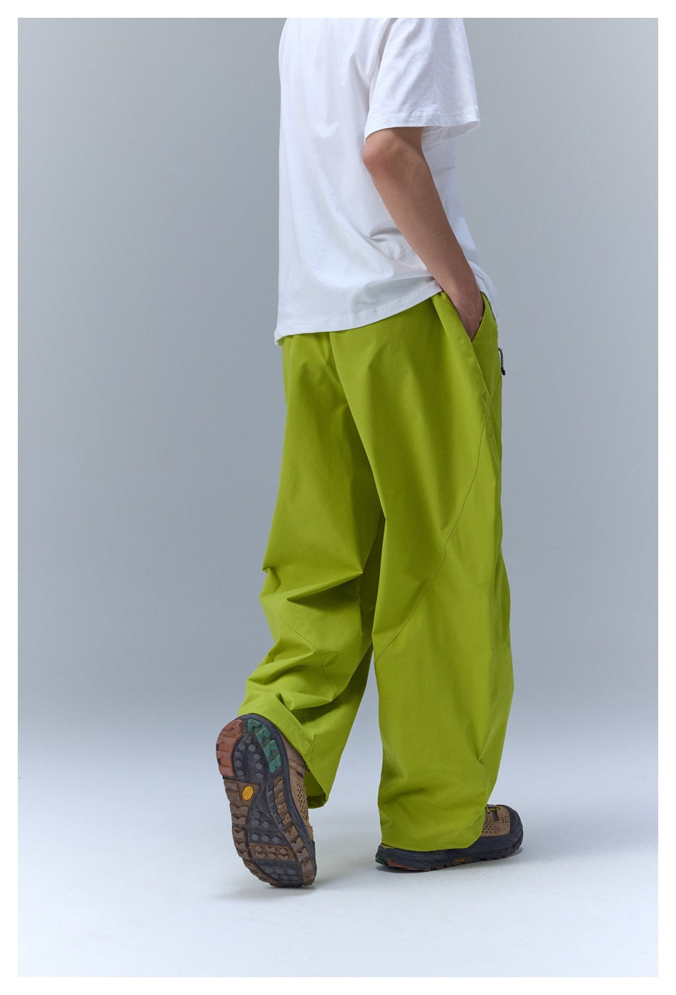 Rear view of a model wearing loose lime-green pants with a white T-shirt and hiking shoes.