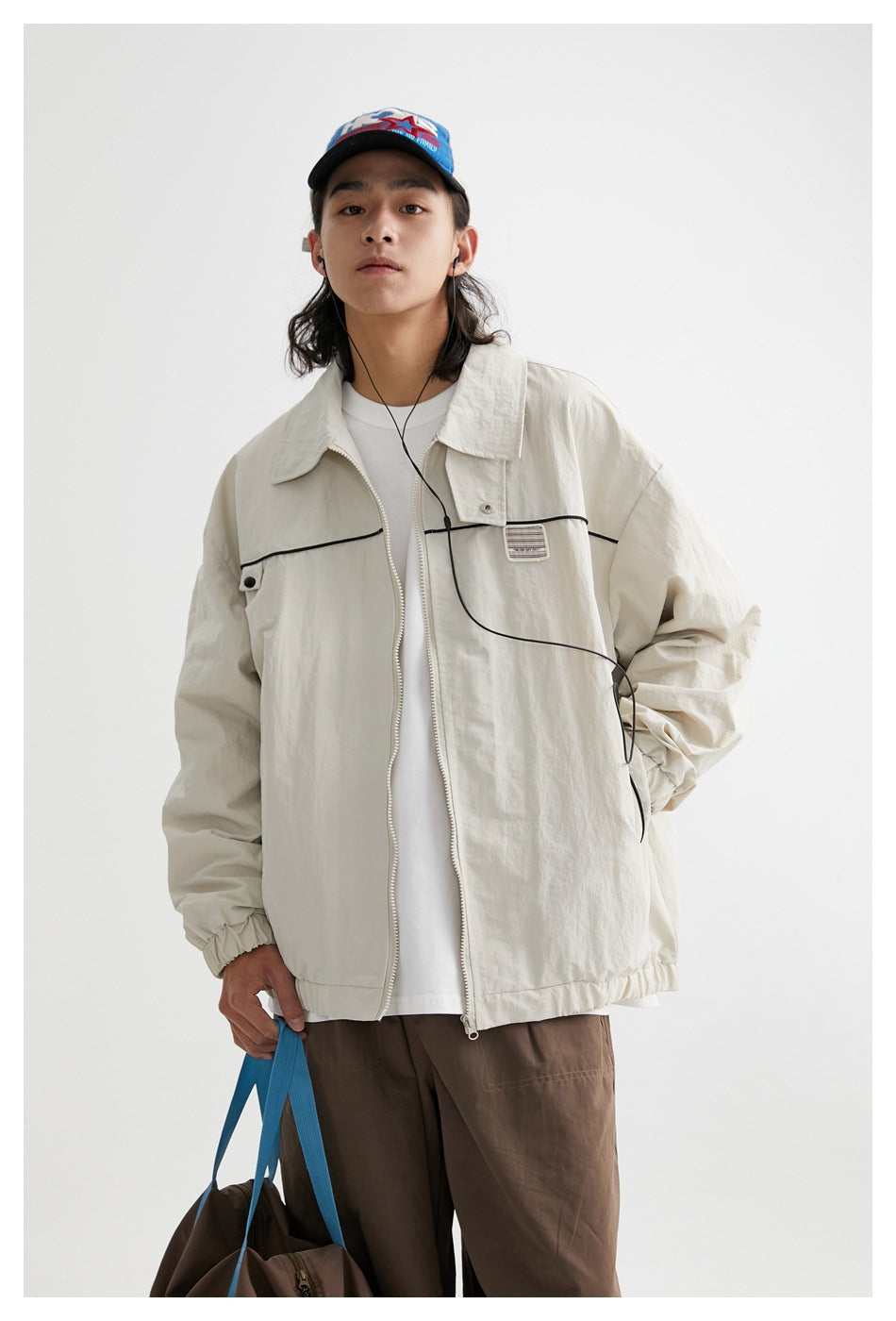 Front view of a model in an ivory zip jacket with black piping and a chest patch, over a white shirt.