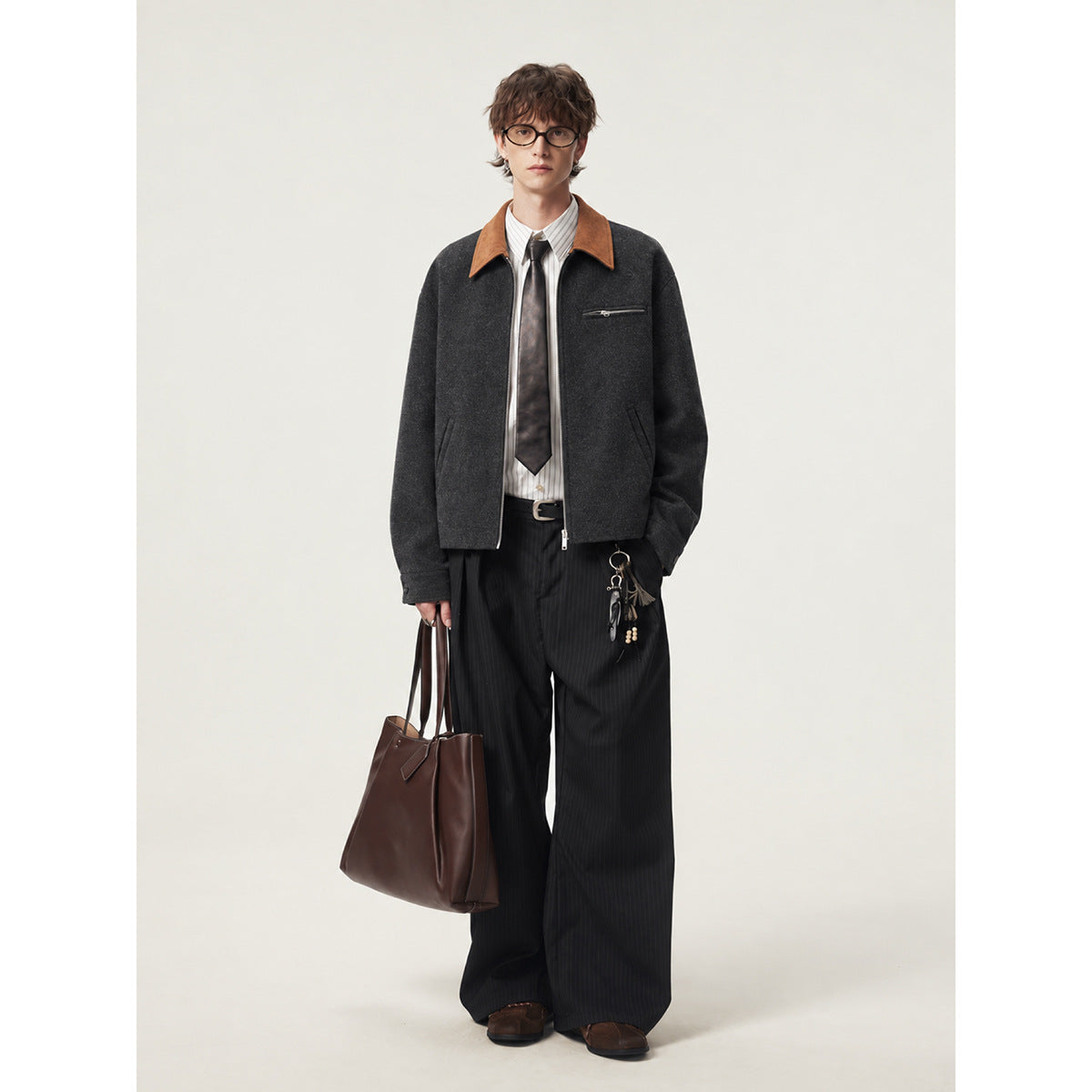 Full-length front view of a model wearing a charcoal jacket with a tan collar, styled with dark pinstripe trousers.