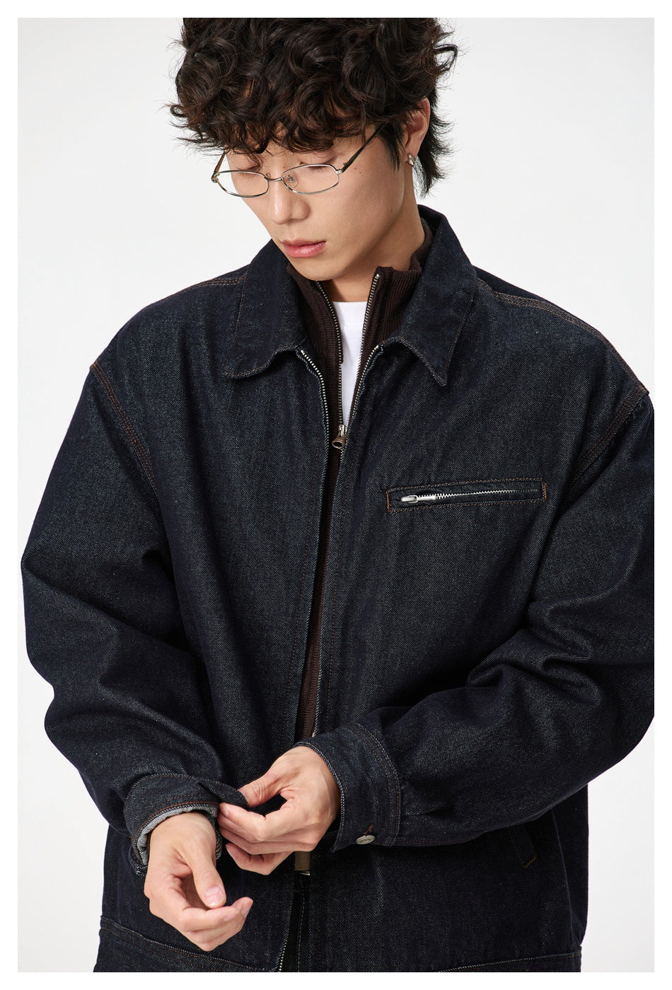 Close-up of a dark indigo denim jacket showing its pointed collar, center zipper and horizontal zip chest pocket.