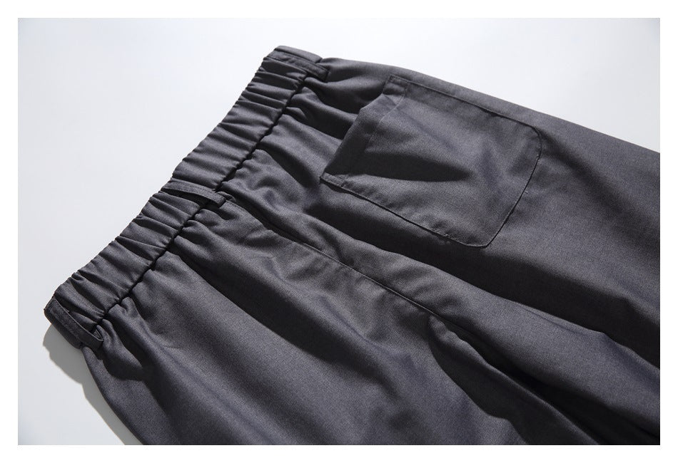 Close-up of charcoal trousers showing a gathered waistband and a rectangular rear pocket.