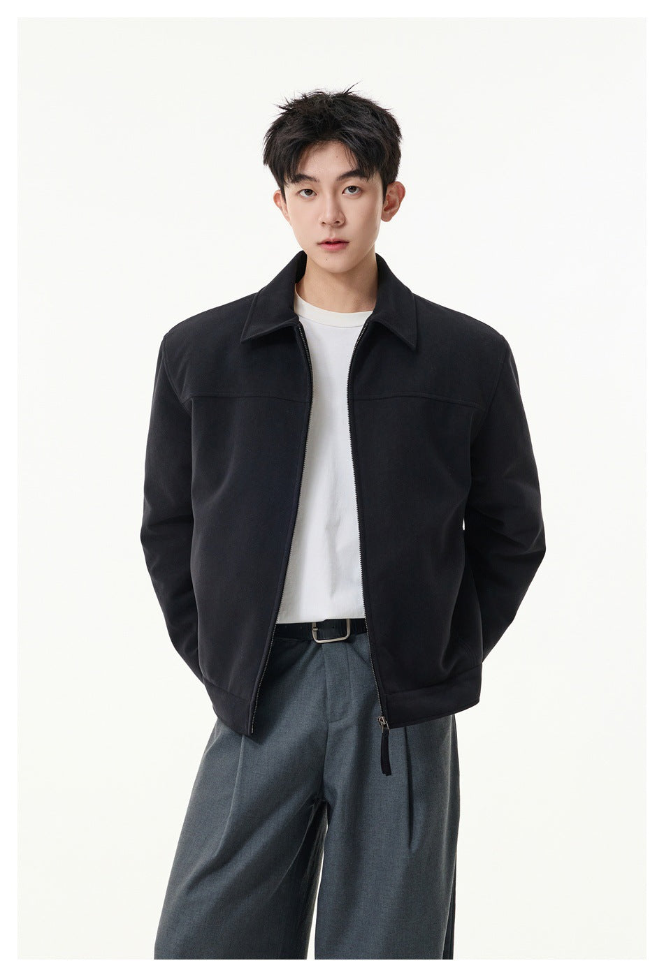 Model wearing an open black collared zip jacket over a white shirt with gray trousers.