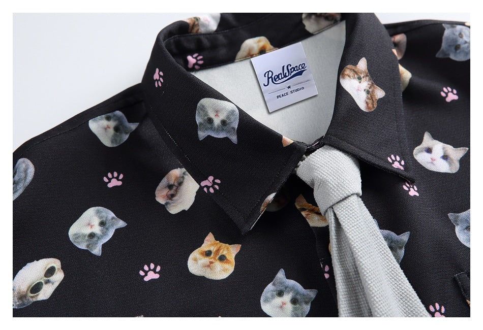 Close-up of a black cat-print shirt collar with a pale gray tie and visible neck label.