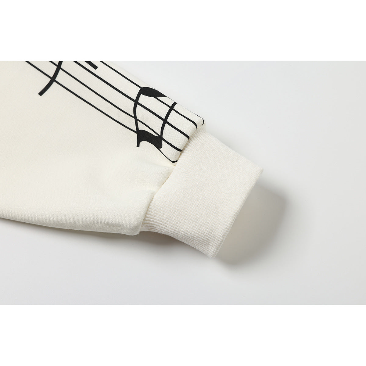 Close-up of an ivory sleeve's ribbed cuff and black musical-staff print.