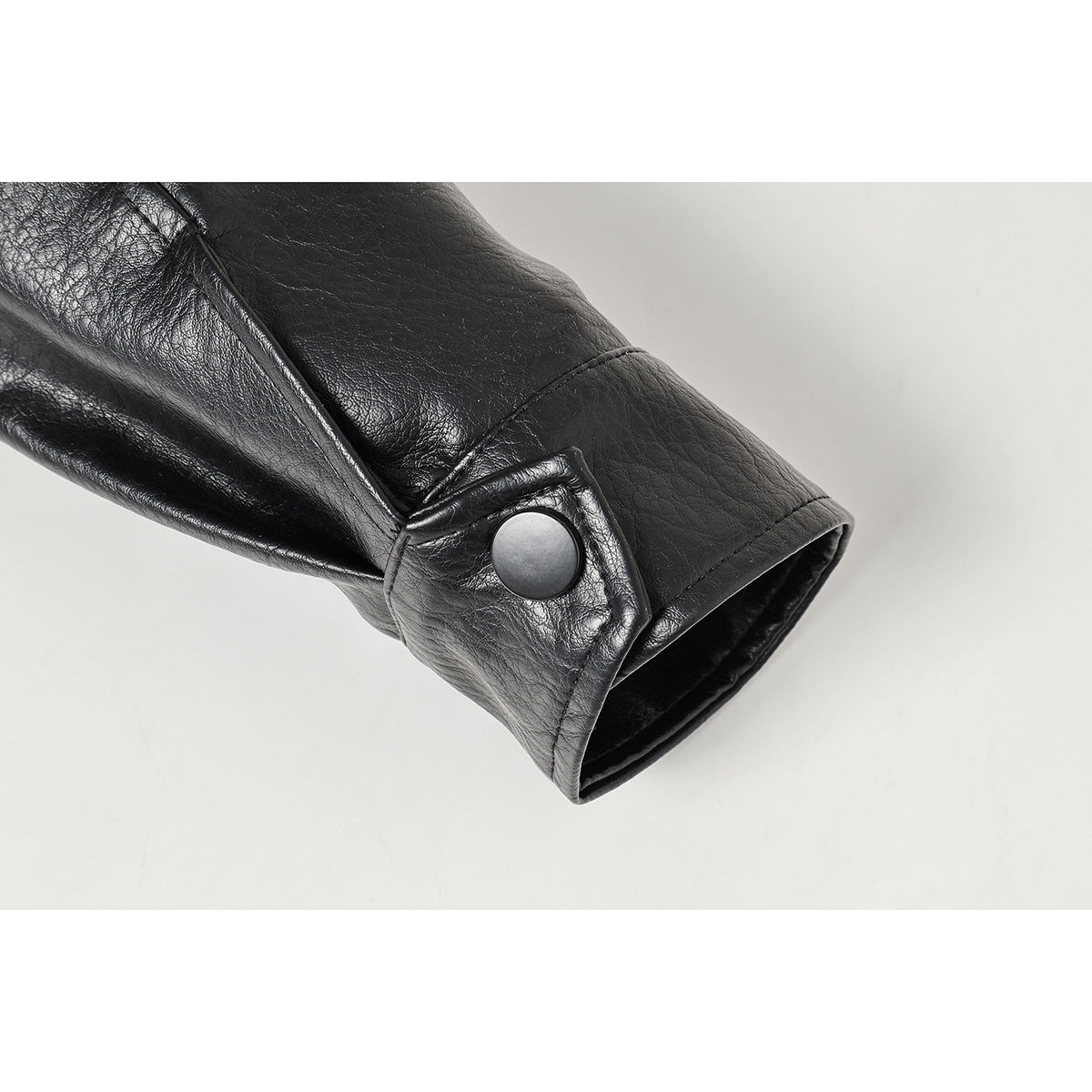 Close-up of a black jacket sleeve cuff with a round snap button and stitched seams.
