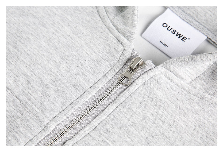 Macro view of a metal zipper and pull on a light gray heather hoodie, beside its sewn-in brand label.