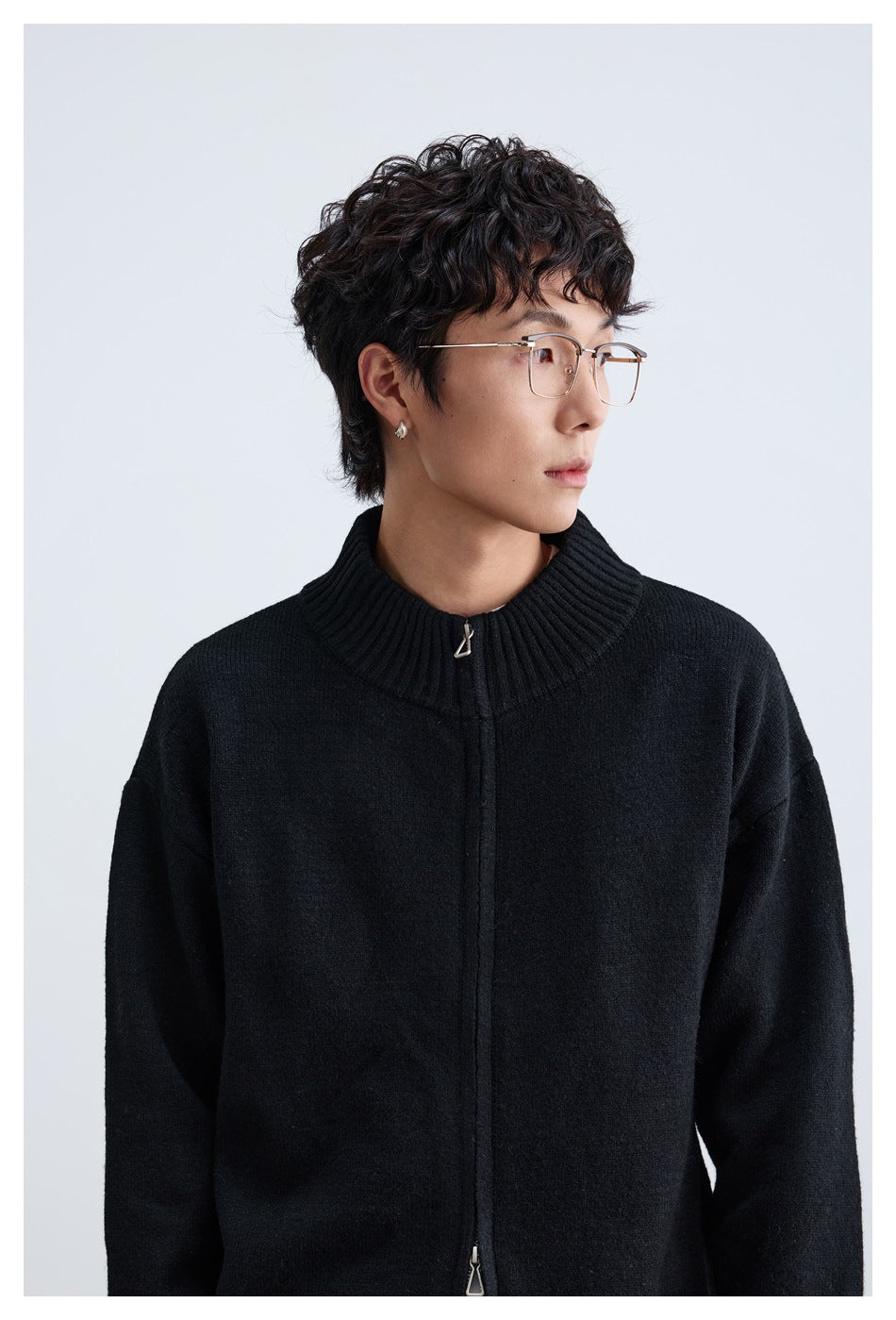 Model in glasses wearing a black zip-up knit cardigan with ribbed stand collar, close-up