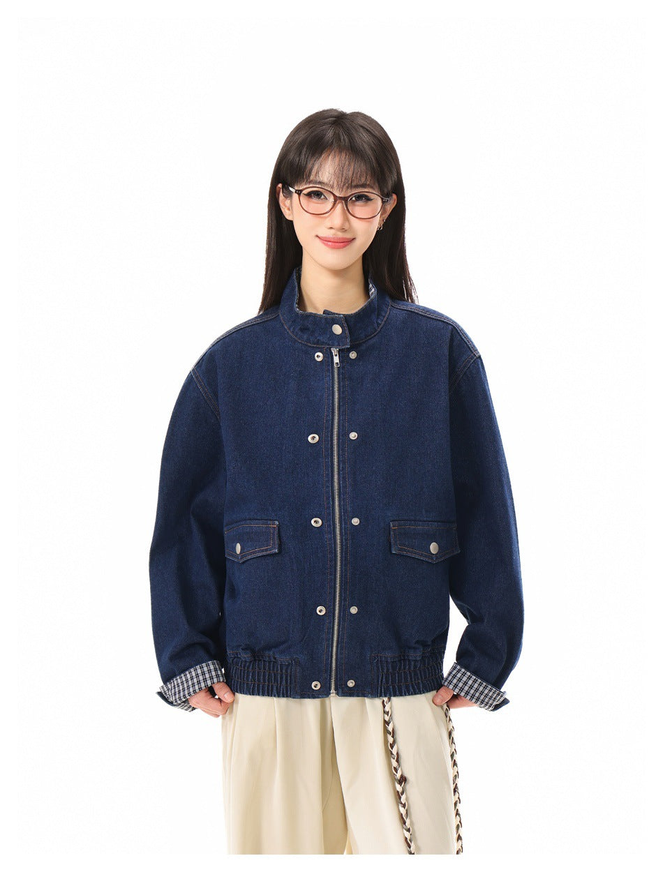 Front view of a model in a dark blue denim jacket with a stand collar, zipper, snap buttons, and checked cuffs.