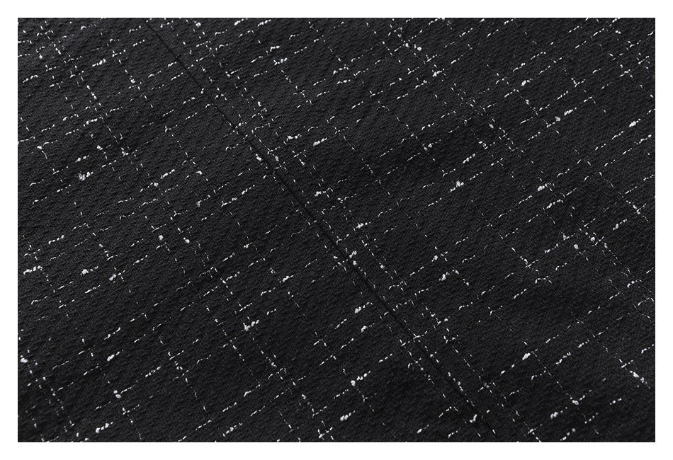 Close-up of black fabric with scattered white flecks and a diagonal seam.