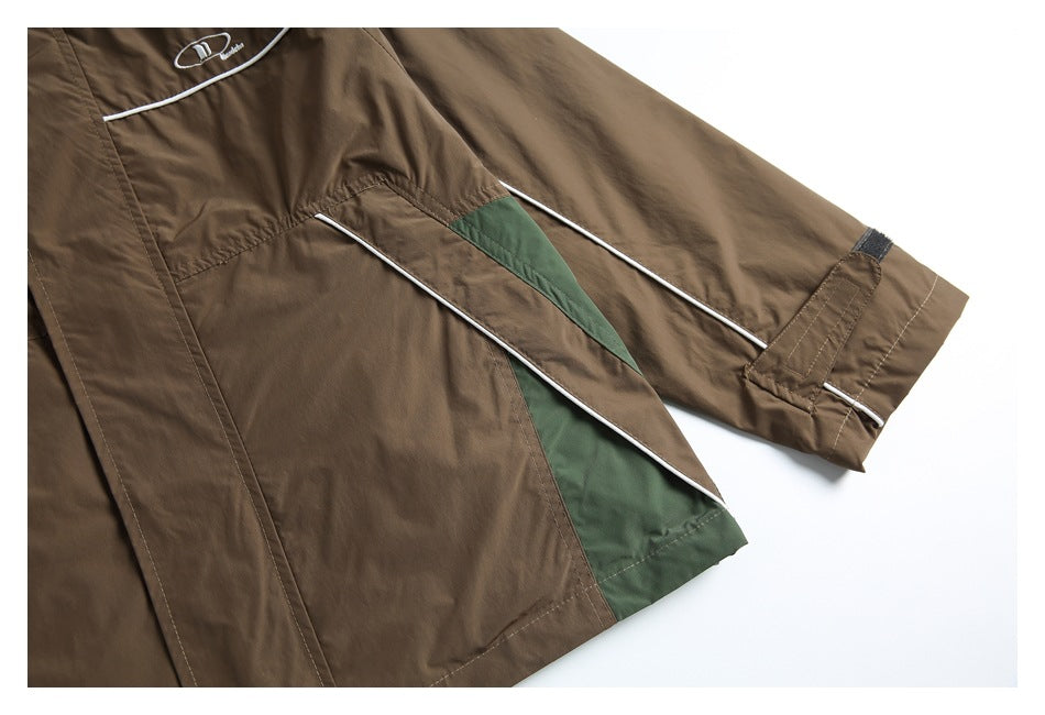 Close-up of a brown jacket's sleeve and side panels, showing green inserts, white piping, and an adjustable cuff.