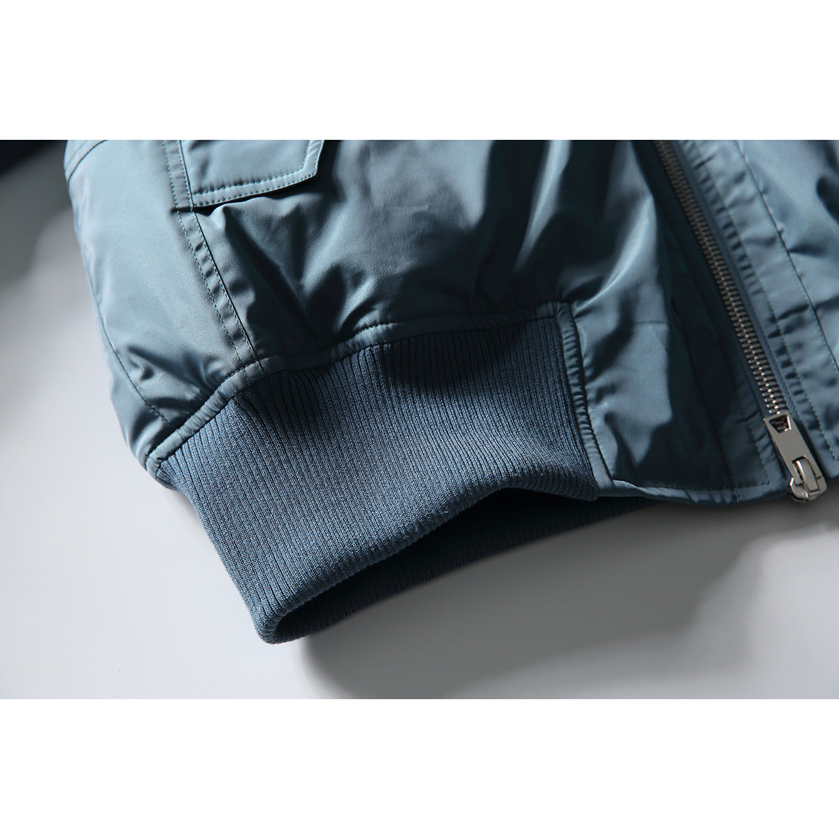 Close-up of the blue jacket's rib-knit hem, flap pocket edge, and front zipper.