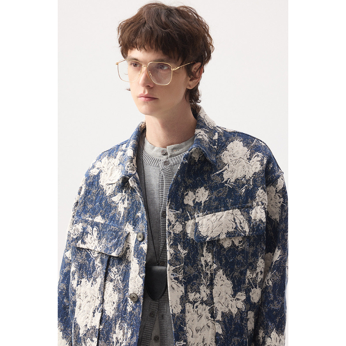 Close view of a model wearing a blue and cream floral-patterned button jacket over a gray cardigan.