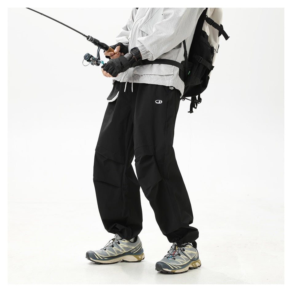 Model wearing loose black cargo pants with layered thigh pockets and gathered ankles while fishing.
