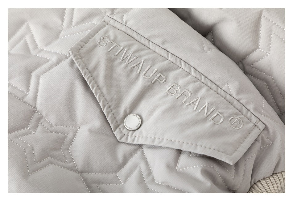 Close-up of a light gray quilted jacket with star stitching, a snap-fastened flap, and embroidered lettering.