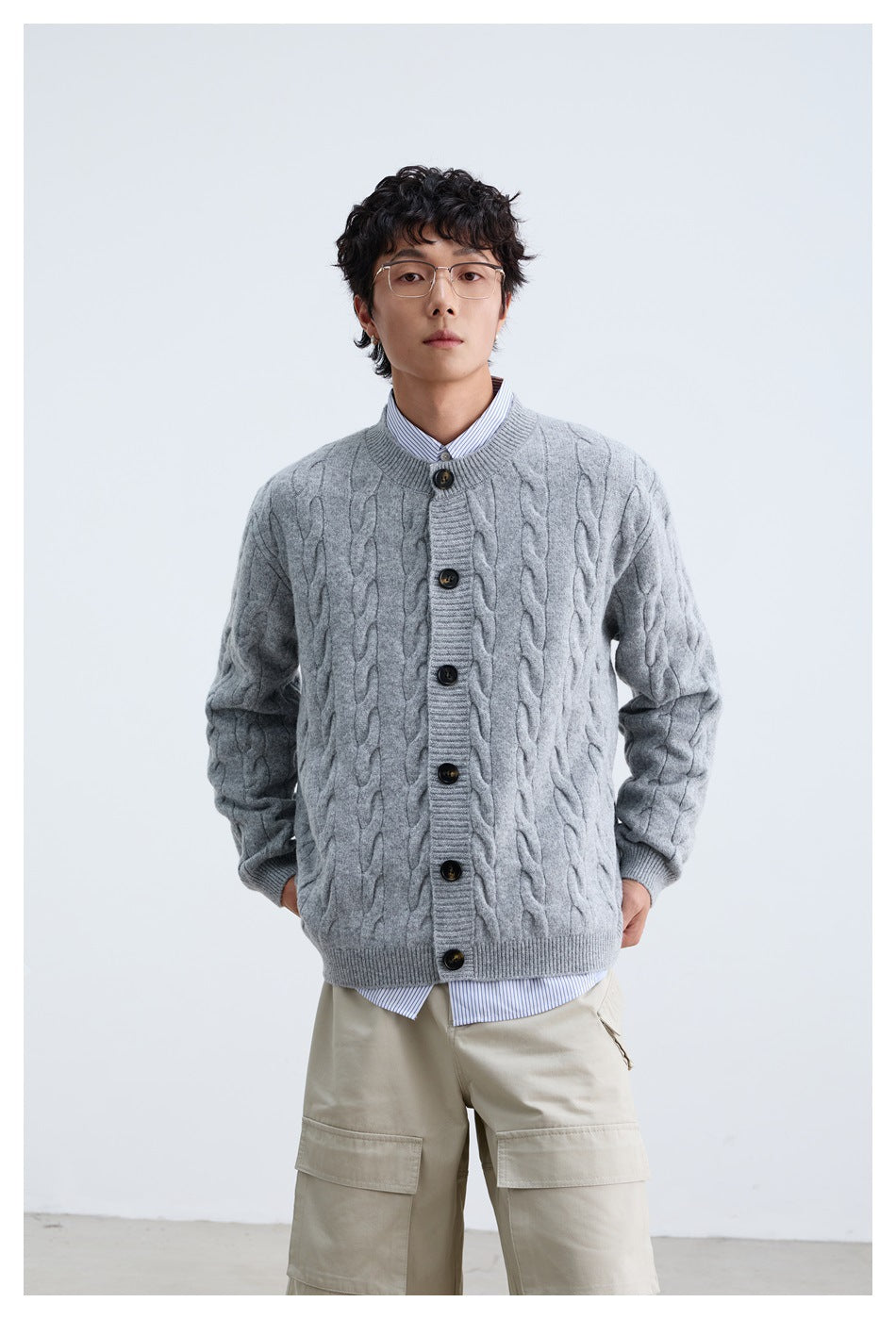 Front view of a person wearing a light gray cable-knit cardigan with dark buttons over a striped shirt.
