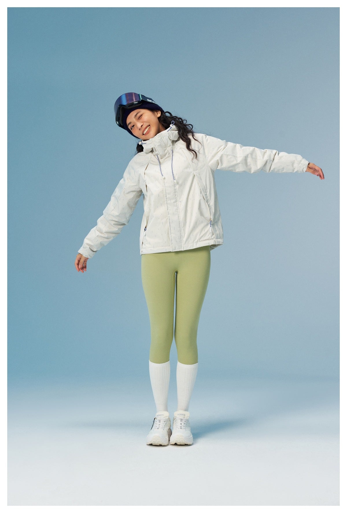 Model wearing a white hooded jacket with fine blue dash pattern and pale green leggings, shown from the front.
