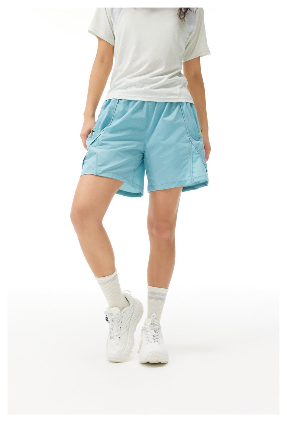 Front view of a model wearing light blue athletic shorts with angled side pockets and a white short-sleeve shirt.