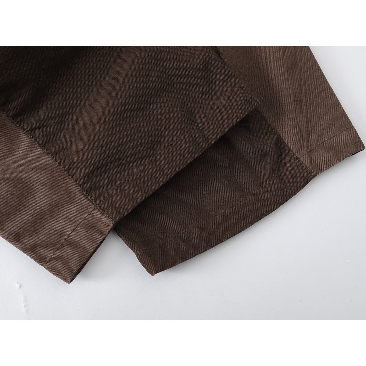 Close-up of the stitched hems and fabric texture of brown trousers.