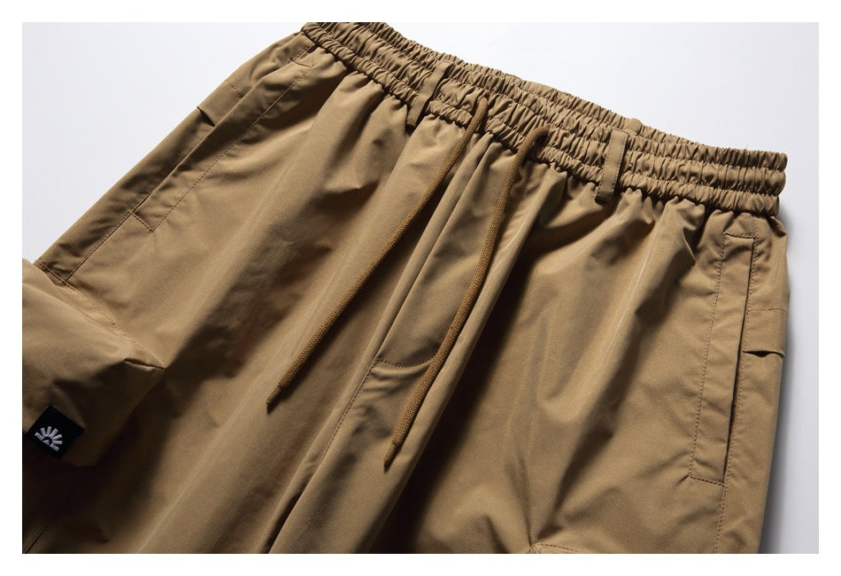 Close-up of tan cargo pants showing the elastic drawstring waist, side pockets, and a small black emblem tab.