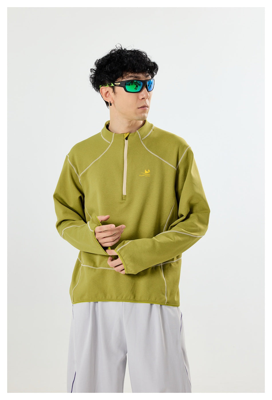 Model wearing an olive-green quarter-zip pullover with contrast seams and extended thumbhole cuffs.
