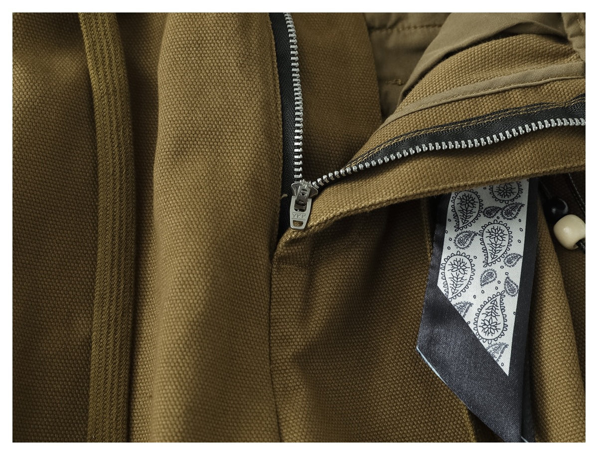 Close-up of olive-brown trouser fabric and a metal zipper beside the paisley-patterned hanging accessory.