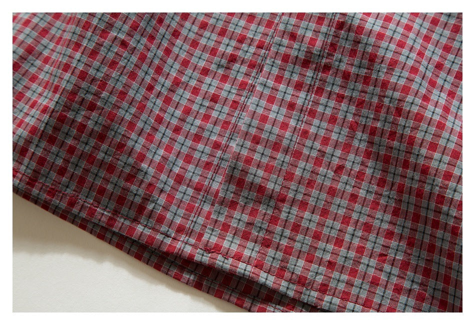 Close-up of the stitched hem of a red, gray, and white plaid shirt.
