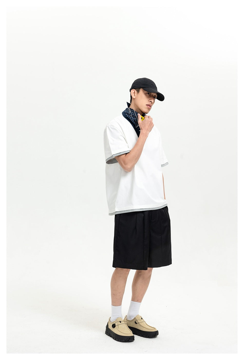 A model wears a white short-sleeve shirt with gray trim, black shorts, a black cap, and beige shoes.