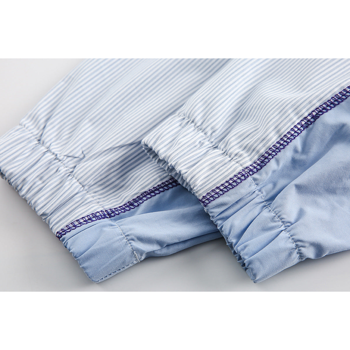 Close-up of striped shirt fabric joined to pale blue fabric, showing gathered seams and dark overlock stitching.