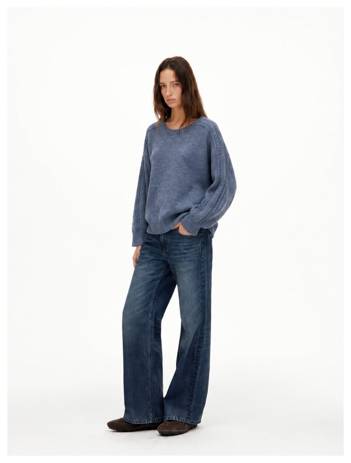 Full-length model wearing a blue-gray cable-sleeve crewneck sweater with wide-leg jeans.