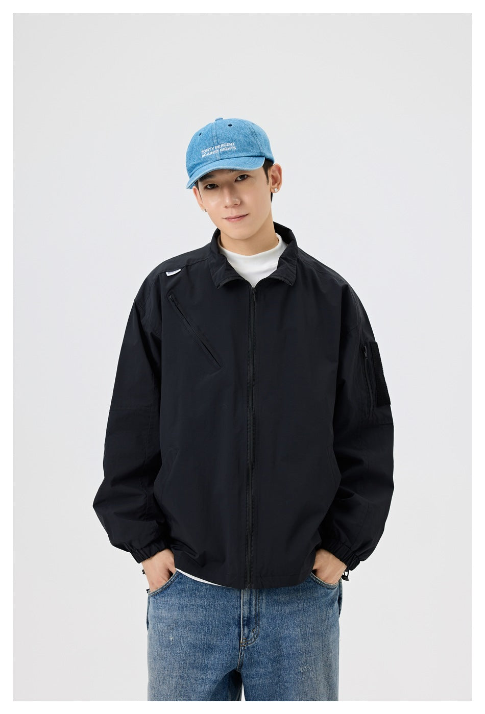 Closer front view of a model wearing a black jacket with a full zipper, high collar and diagonal chest pocket.