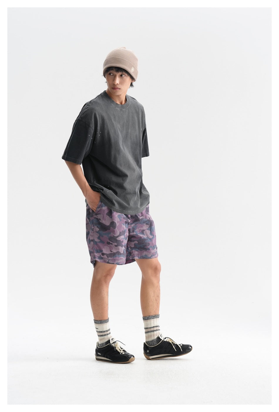 Three-quarter view of a model in a charcoal oversized T-shirt and purple camouflage shorts.